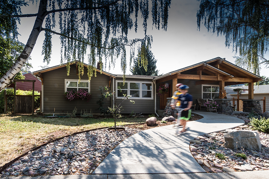 Two boys become a blur as they scooter along a snaking accessible pathway away from a green house.